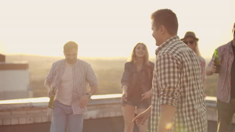 A-young-man-in-a-gray-plaid-shirt-moves-in-dance-with-his-friends.-He-enjoys-and-has-fun-with-beer-on-the-roof.